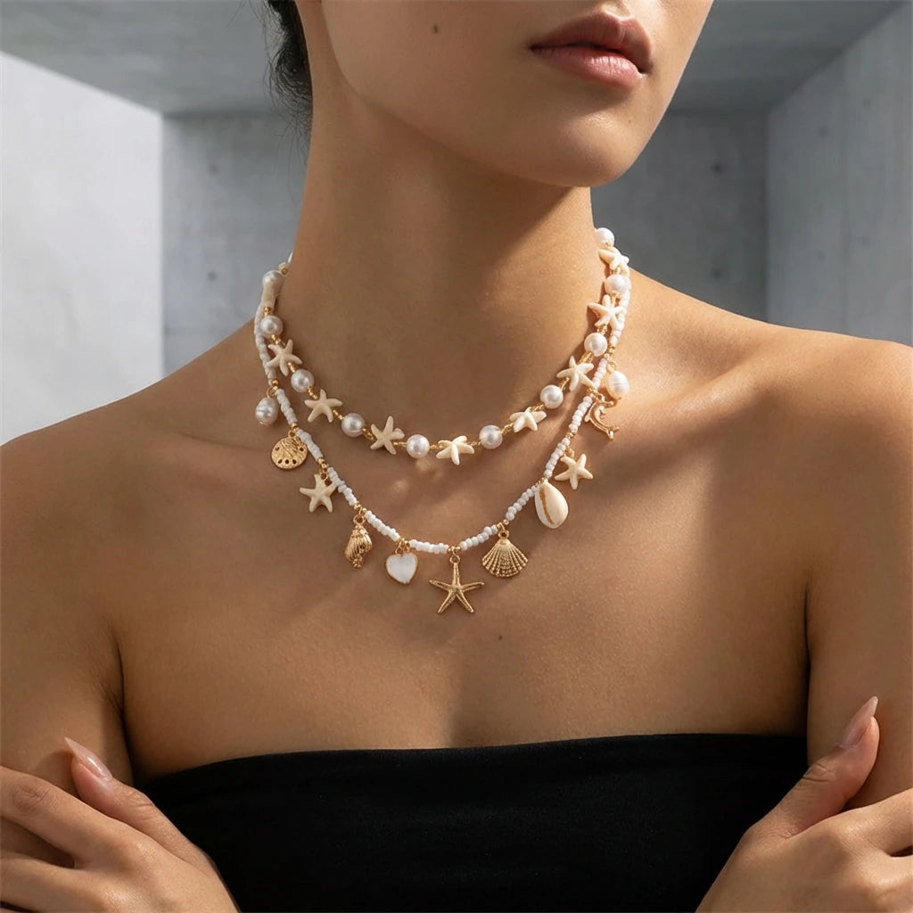 A close-up of a woman wearing a delicate gold and pearl boho shell starfish necklace.