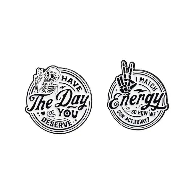 Black enamel lapel brooch featuring a skull and hand design with the text Have The Day You Deserve and Match Energy
