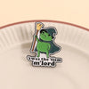 Un pin de esmalte con una rana verde usando un sombrero de mago y sosteniendo una escoba sobre un plato de cerámica rosa clar