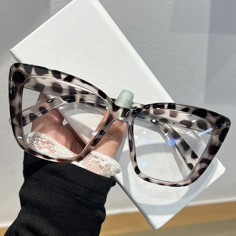A hand holds a pair of tortoiseshell cat eye sunglasses against a white background.