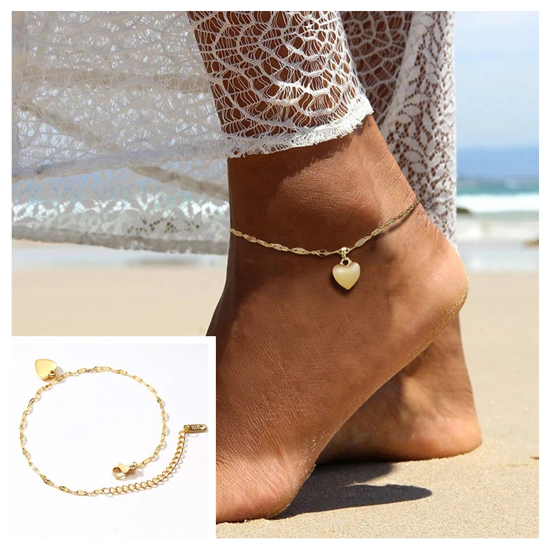 A close-up of a gold stainless steel snake chain anklet worn on a woman's foot near the ocean.