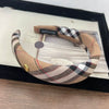 A beige and black plaid fabric headband displayed in a black frame.