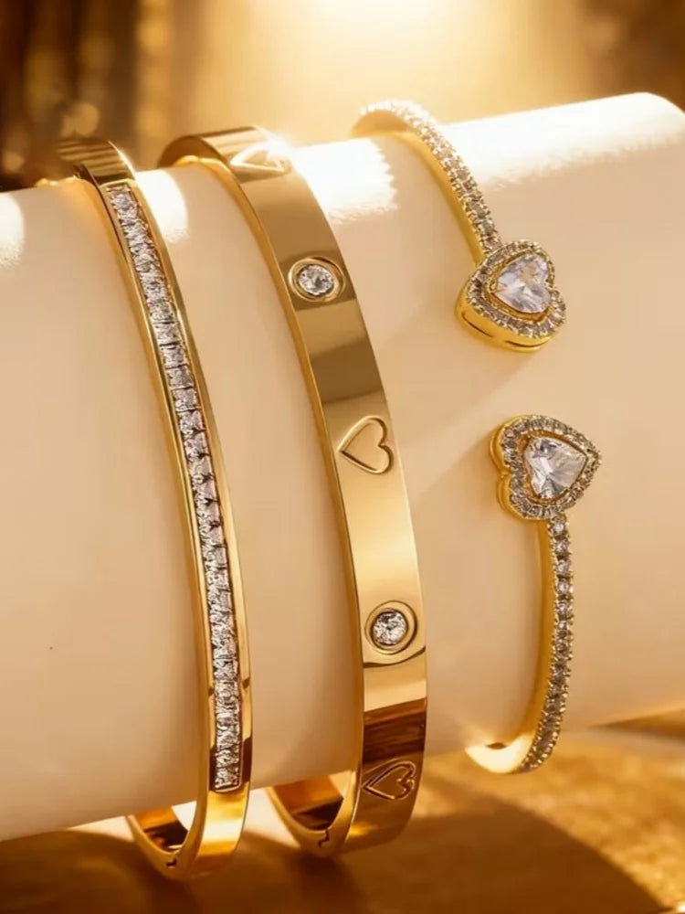 Ein Set aus drei 18K goldvergoldeten Edelstahlherzarmbändern mit Diamantbesatz auf hellem Hintergrund.