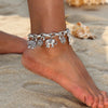 A close-up of a vintage gold elephant charm bracelet worn on a wrist, resting on sandy beach ground.