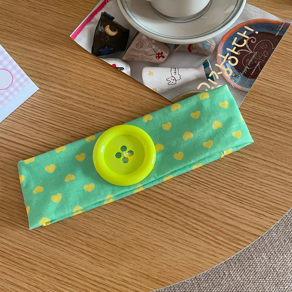 A bright lime green headband with yellow polka dots is displayed on a wooden table next to various small items.
