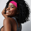 A woman smiling while wearing a bright pink wig cap and a dark, textured top.