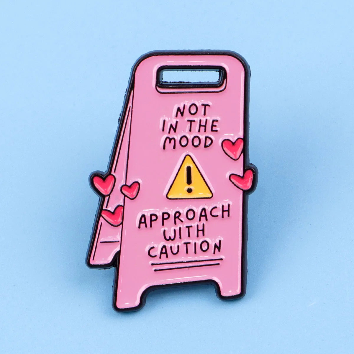 Pin de esmalte rosa con un triángulo de precaución amarillo y el texto: 'No estoy de humor, acérquese con precaución'.