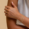 A close-up of a hand wearing a stack of dainty gold plated bracelets on the wrist.