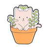 A cute pink cat face peeking out of an orange pot with green leaves, designed as an enamel flower brooch set.