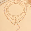 A gold layered necklace featuring a pearl cross pendant and delicate chains, displayed on a light background.