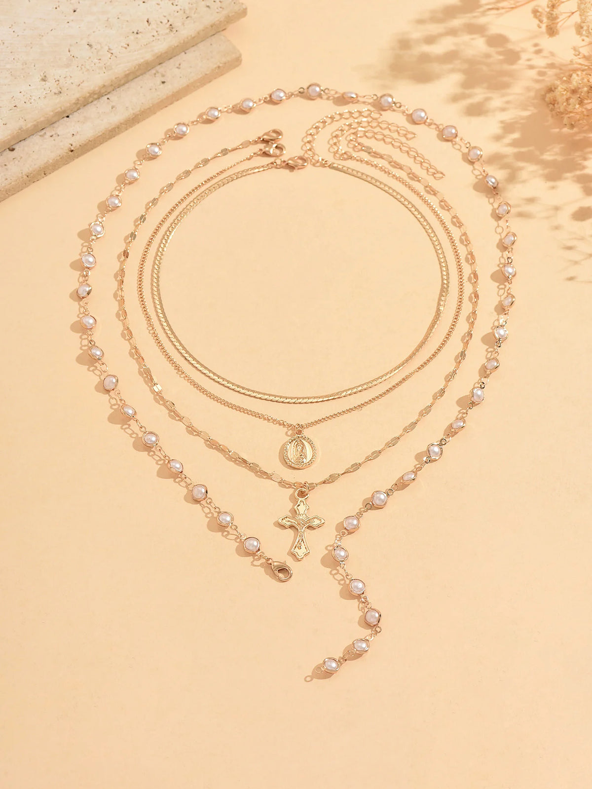 A gold layered necklace featuring a pearl cross pendant and delicate chains, displayed on a light background.