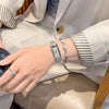 A close-up of a woman's wrist wearing several silver and gold watches and bracelets, next to a light beige blazer.
