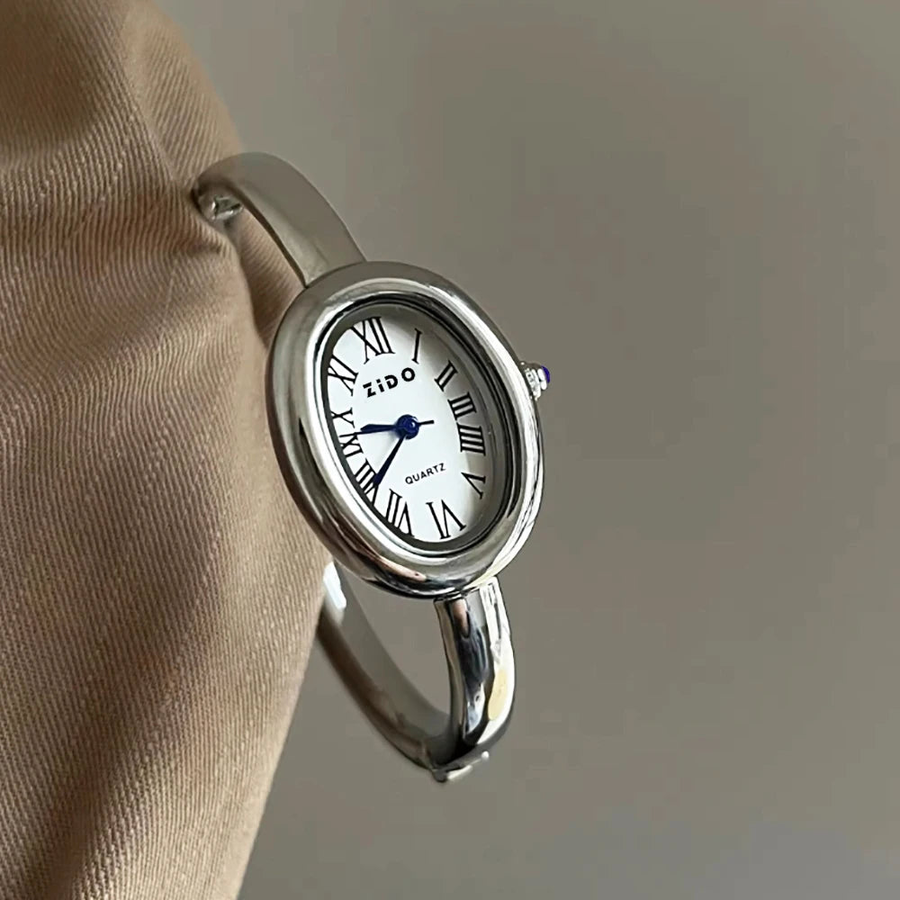A silver ZIDO quartz analog watch with an oval face is shown on a wrist.