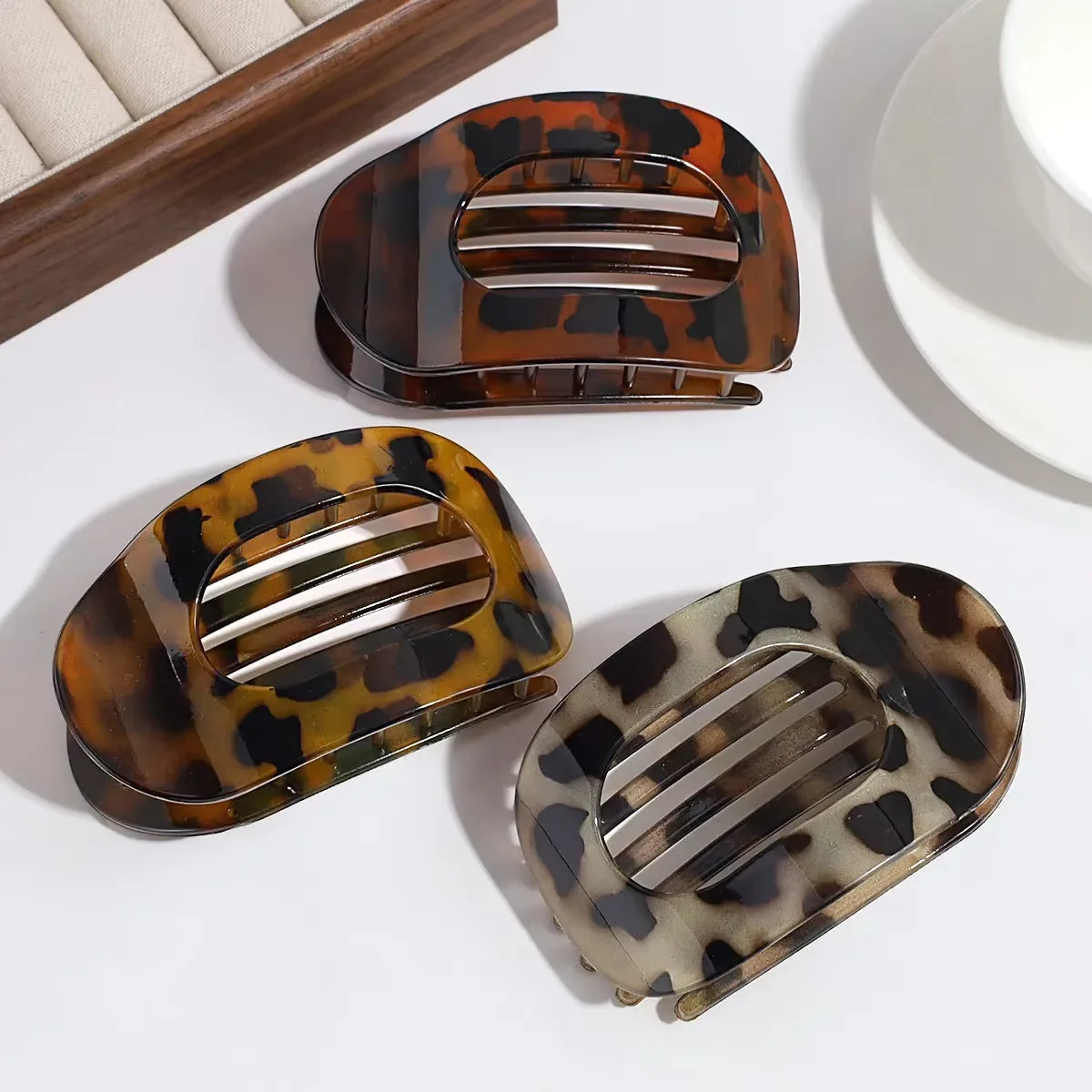 A matte leopard print oval hair claw clip in brown and black spots, shown against a white background.