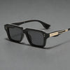 Ein Paar schwarze retro quadratische Metall-Sonnenbrille mit goldenen Akzenten auf einer grauen Oberfläche.