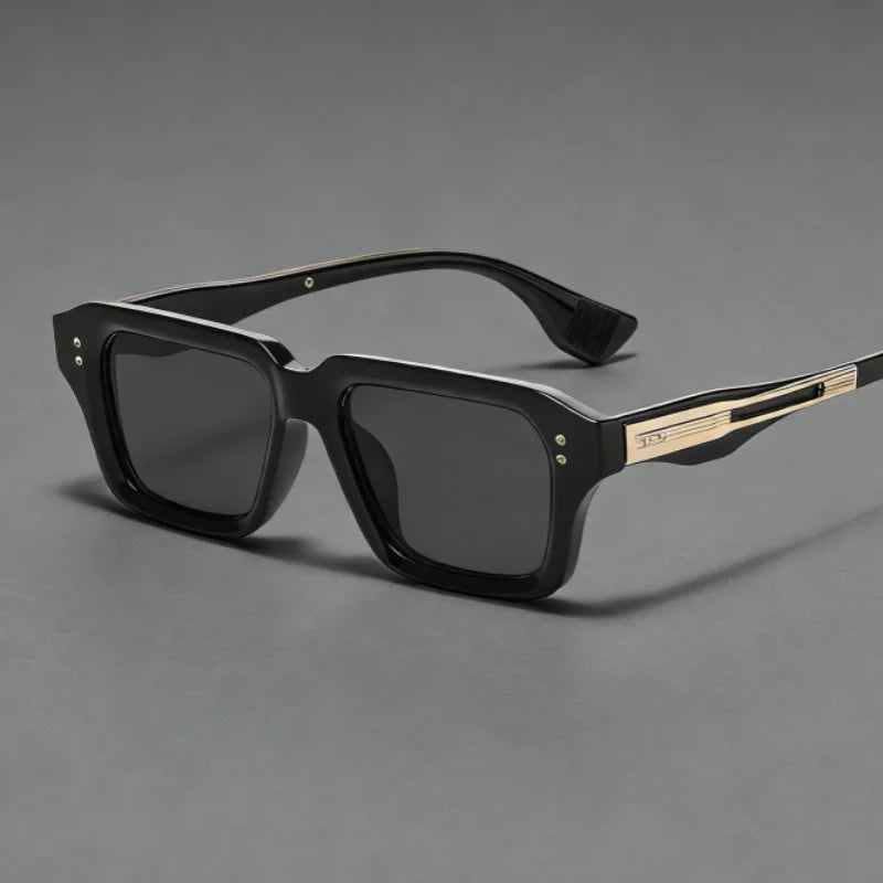 Ein Paar schwarze retro quadratische Metall-Sonnenbrille mit goldenen Akzenten auf einer grauen Oberfläche.