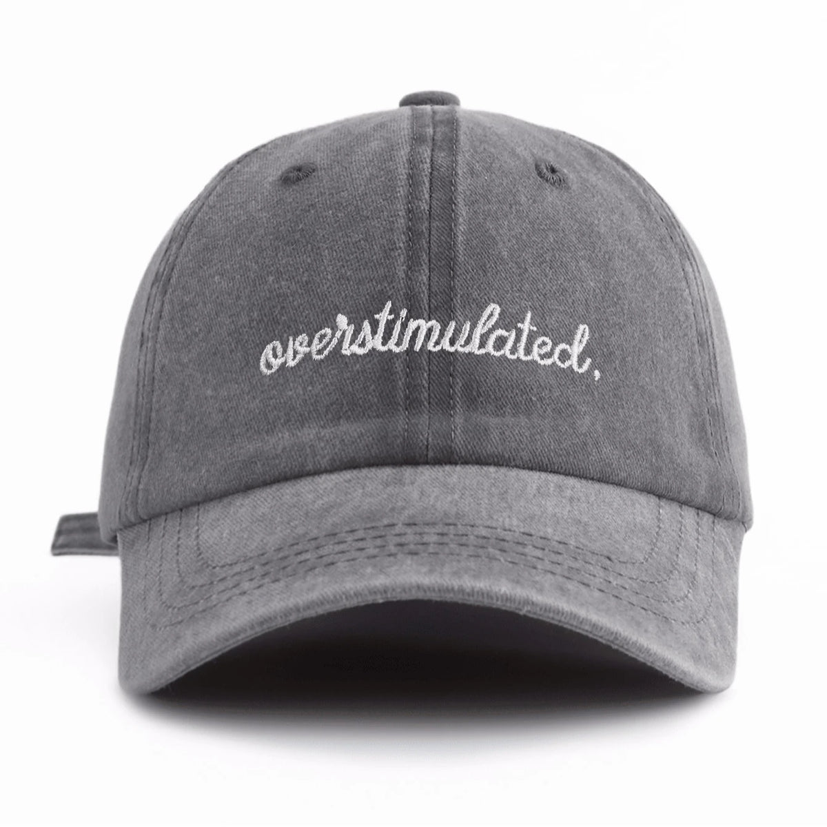 A gray washed baseball cap with white embroidered text that reads overstimulated