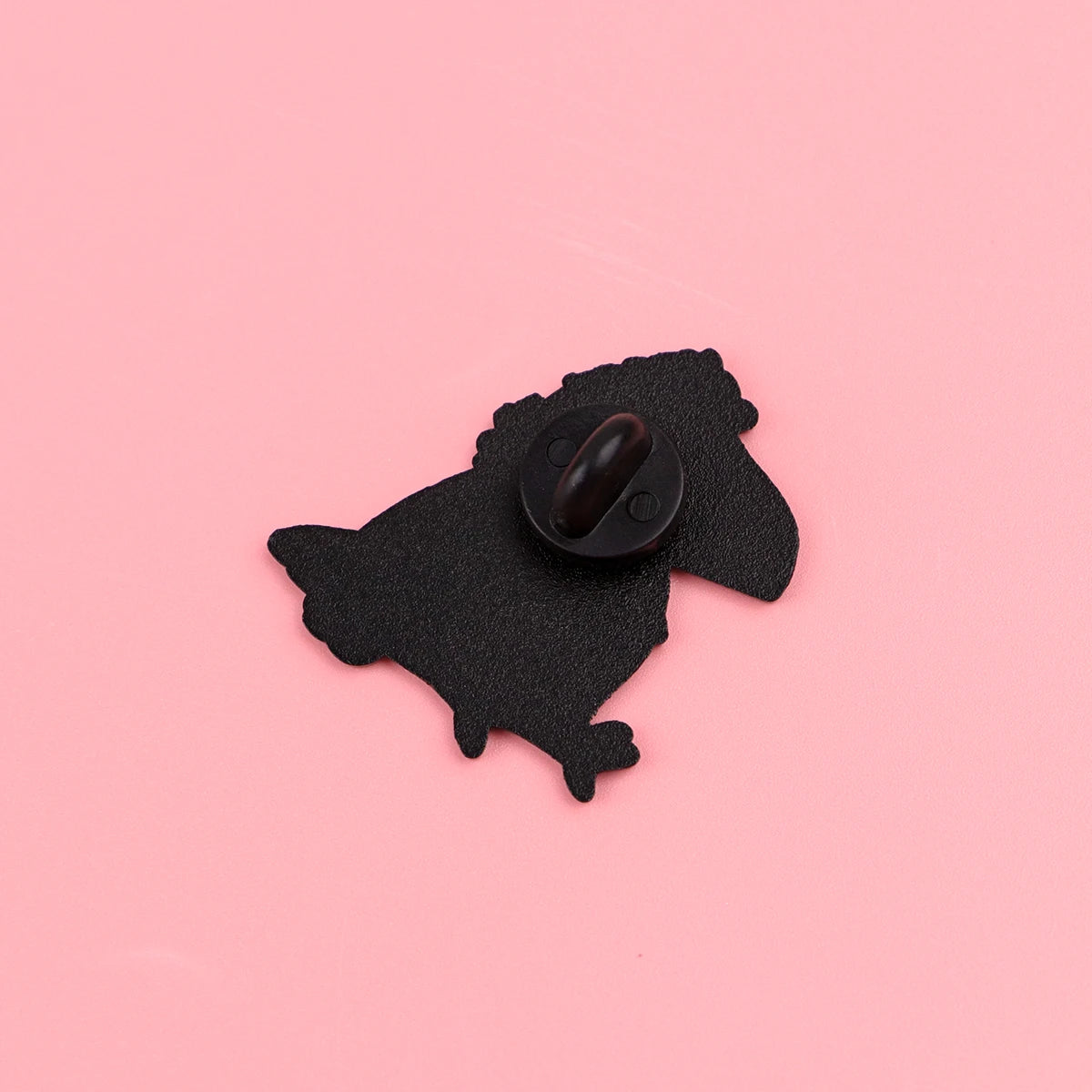Schwarze Silhouette einer Krähe auf rosa Hintergrund, mit einer Emaille-Anstecknadel.