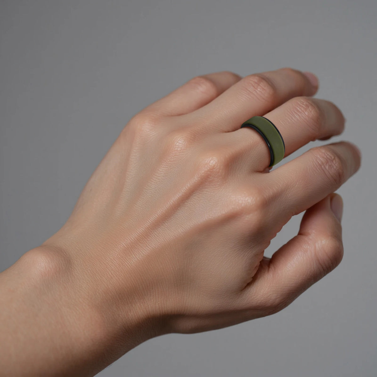 A hand wearing a dark olive green silicone wedding band on the ring finger.