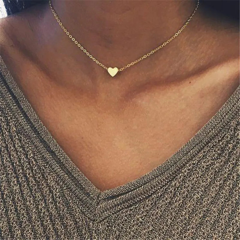 Rapproché d'un collier minimaliste en or avec un petit charm cœur porté autour du cou.