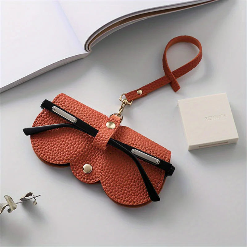 An orange PU leather pouch and glasses case with a leather strap is displayed on a white surface.