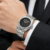 A close-up of a stainless steel watch with a black dial and silver bracelet worn on a wrist next to a suit jacket.