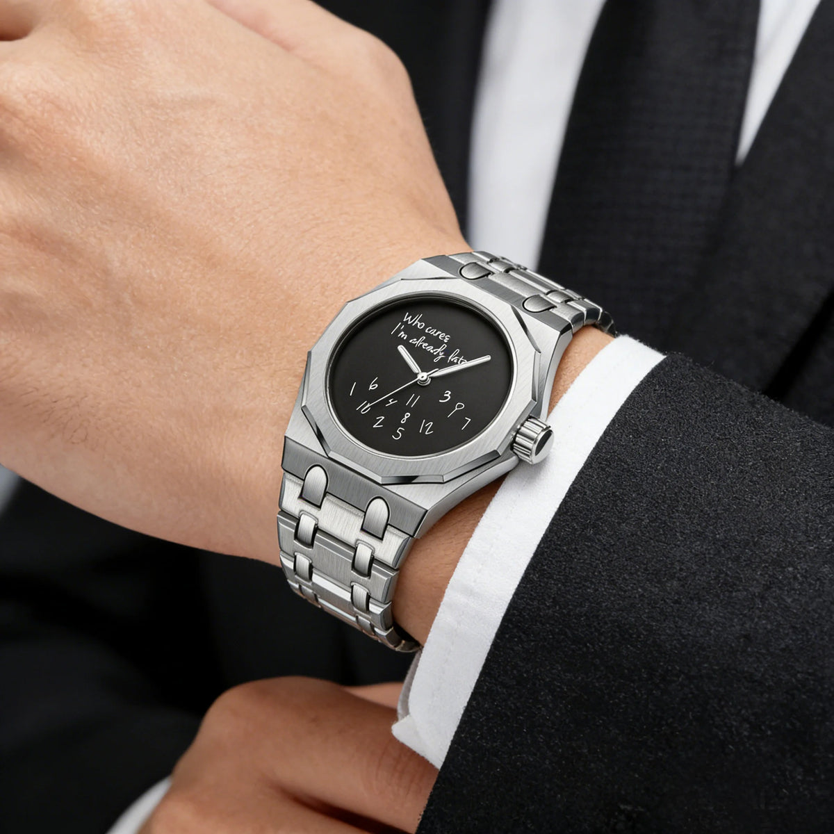 A close-up of a stainless steel watch with a black dial and silver bracelet worn on a wrist next to a suit jacket.