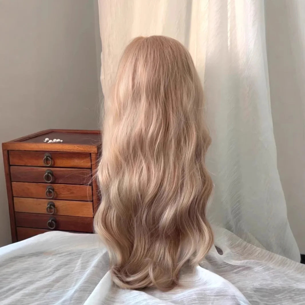 Una larga peluca de cabello rubio ondulado y sintético, exhibida contra una sábana blanca con una caja de madera de fondo.