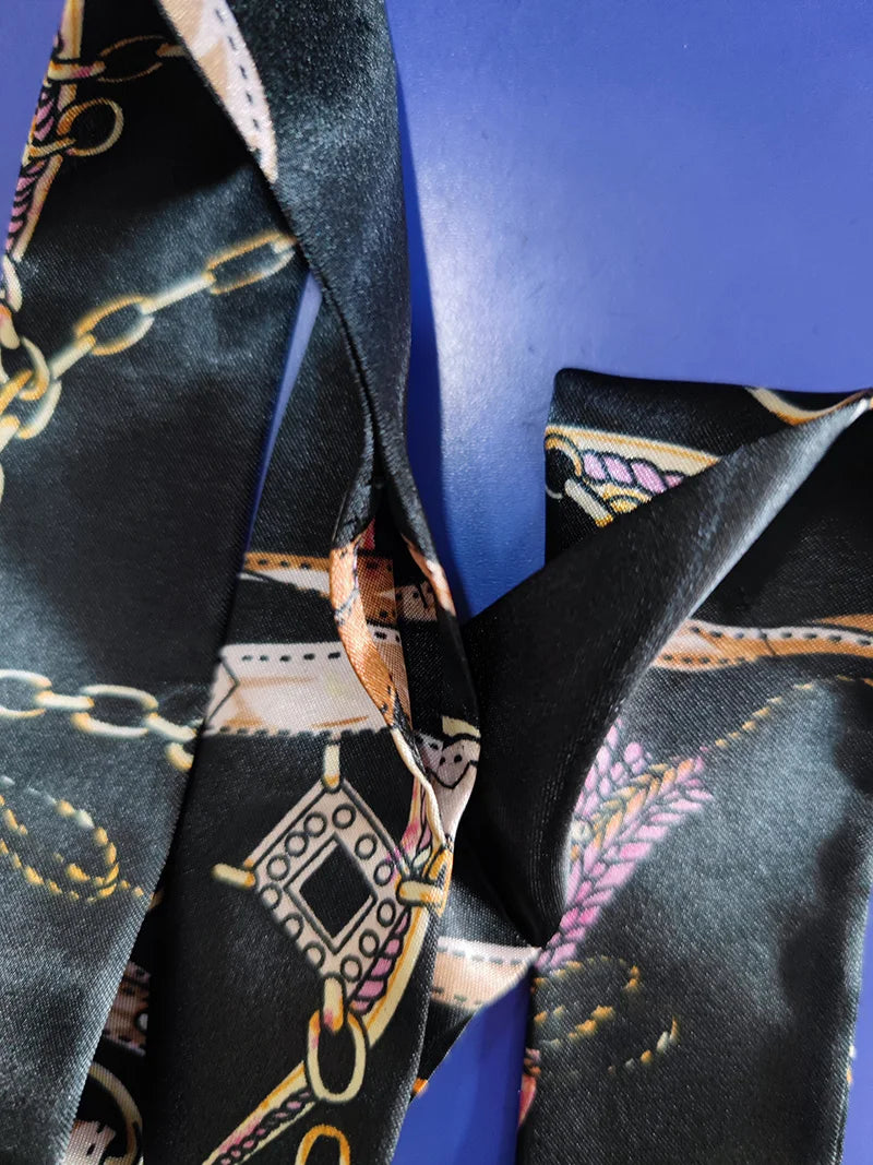 A close-up of a black silk scarf with multi-color leopard print and gold chain detailing.