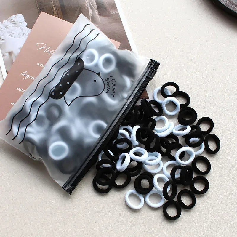A pile of black and white elastic hair bands is shown next to a packaged product featuring a cat design.