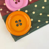 A vintage polka dot button headband featuring a bright orange button and a deep green fabric.