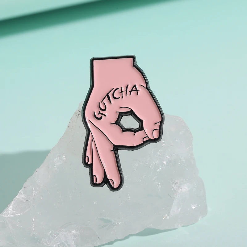 دبوس ميدالية من الإنميل وردي على شكل قبضة مكتوب عليها GETCHA، مستقر على قطعة ثلج شفافة.
