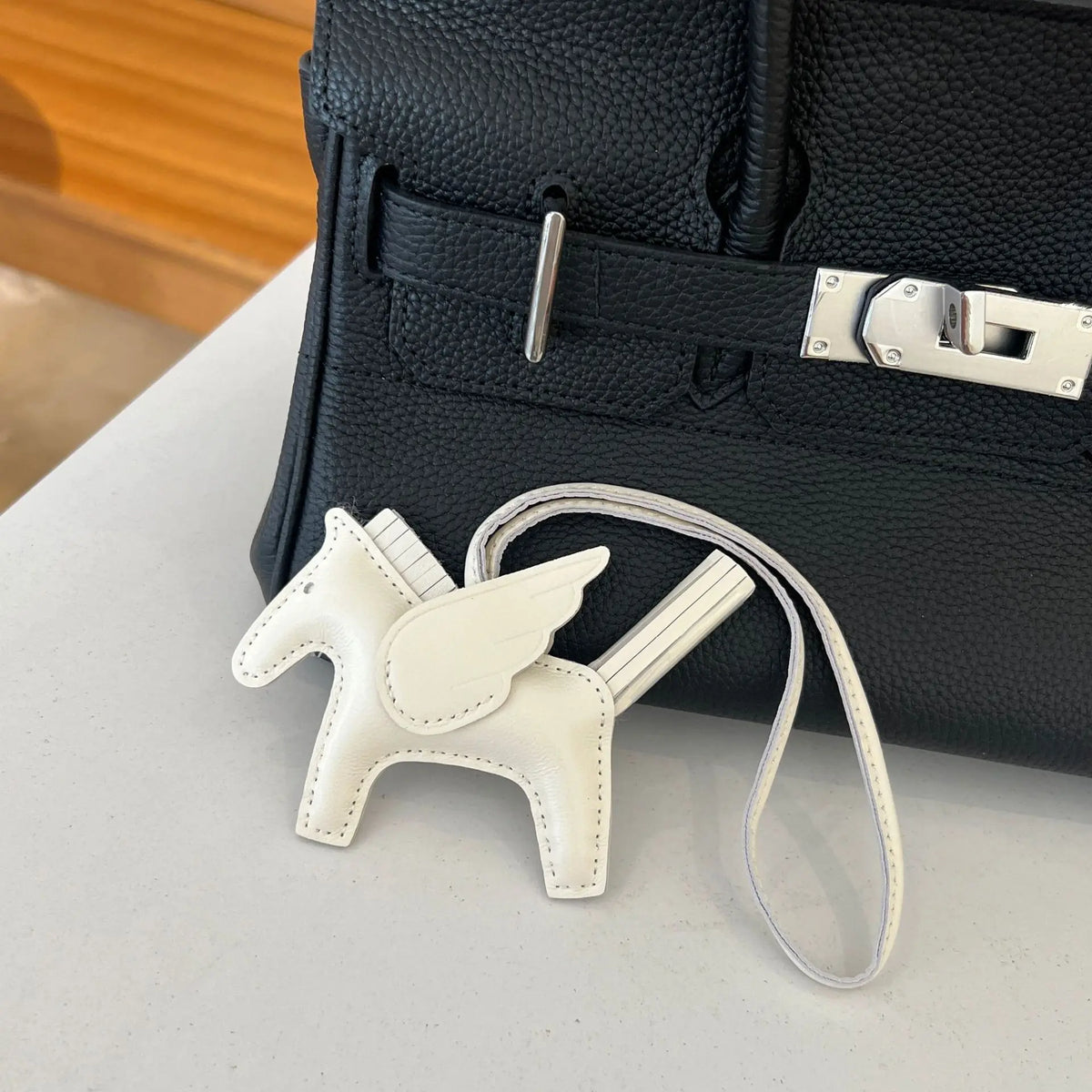 A white horse pendant charm is displayed in front of a black leather bag.