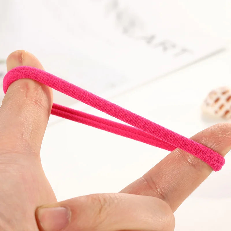 A hand holds a bright pink elastic hair rope, demonstrating its flexibility and texture.