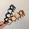 A close-up of a brown resin wave toothed headband for women, featuring black and amber colored plastic teeth.