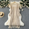 A beige knitted shawl cardigan draped over a white fluffy fur rug with white flowers.