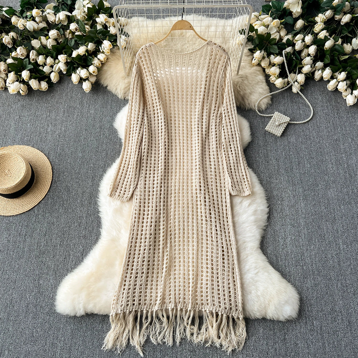 A beige knitted shawl cardigan draped over a white fluffy fur rug with white flowers.
