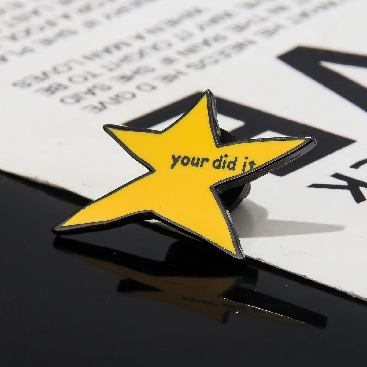 A yellow star shaped enamel pin with the text your did it on a black surface.