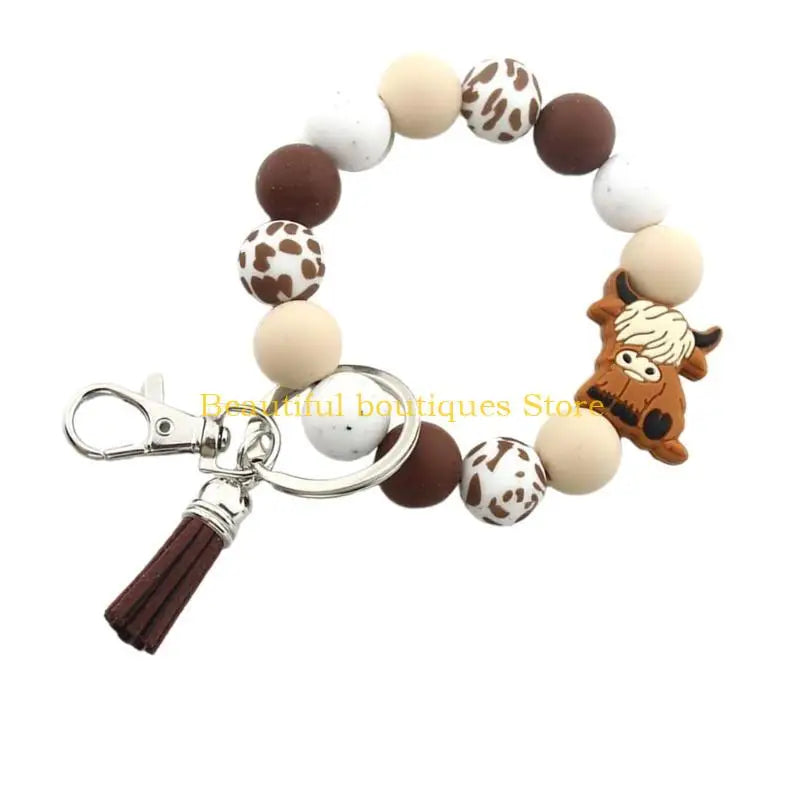 A silicone wristlet keychain featuring round beads in brown, white, and tan colors with a Highland cow charm.