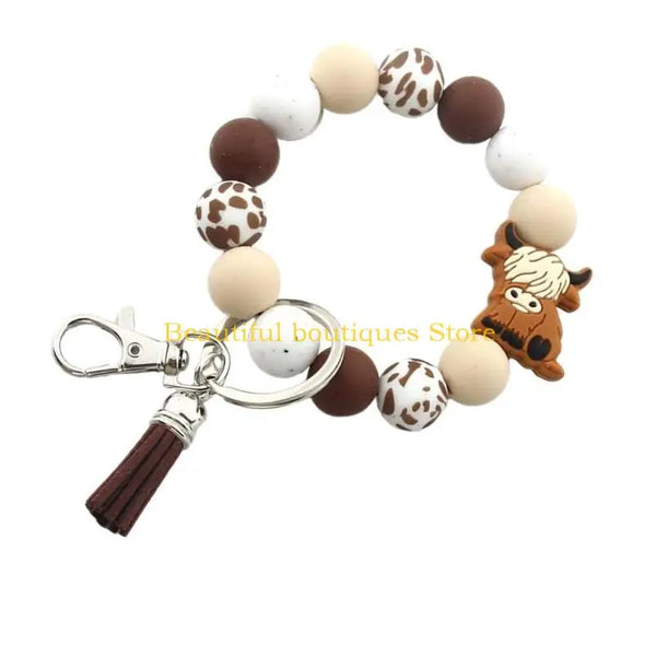 A silicone wristlet keychain featuring round beads in brown, white, and tan colors with a Highland cow charm.