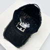 A black baseball cap with a distressed texture and a silver embroidered letter on the front.