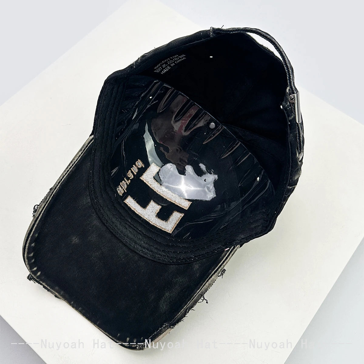 A black baseball cap with a distressed texture and a silver embroidered letter on the front.