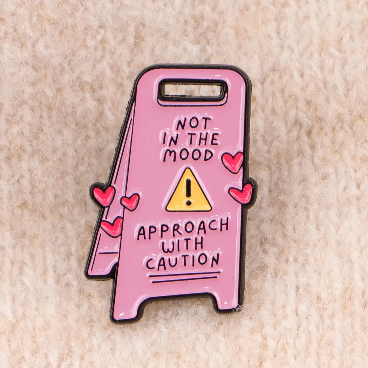 Insignia de esmalte rosa con una señal de advertencia y el texto 'Acérquese con precaución'