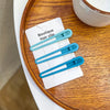 A set of three light blue vintage frosted geometry hair clips displayed on a white card on a wooden plate.