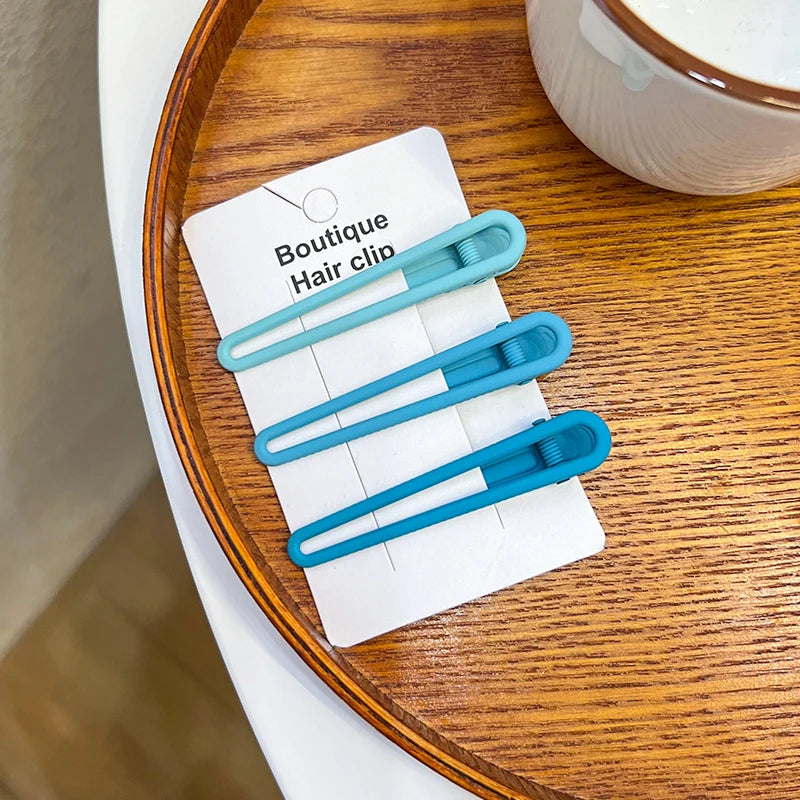 A set of three light blue vintage frosted geometry hair clips displayed on a white card on a wooden plate.