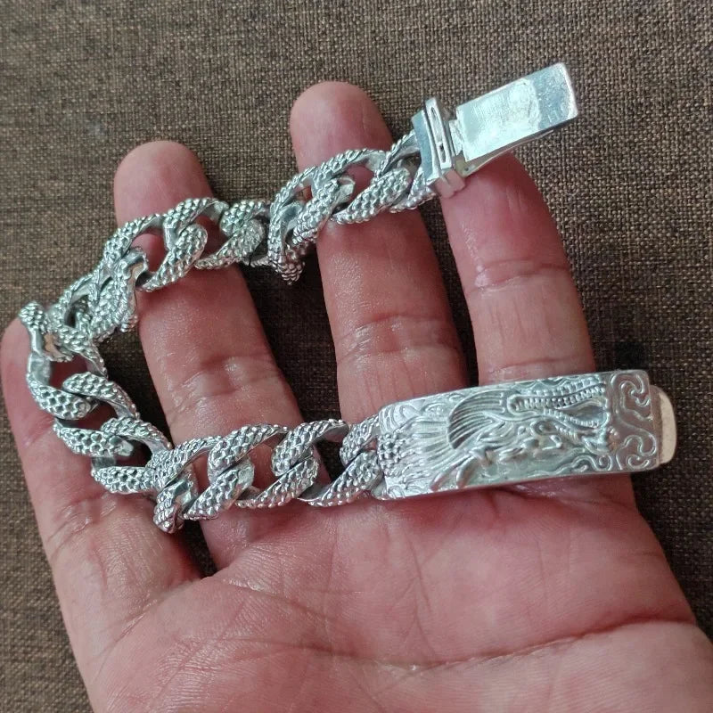 Eine Hand hält ein Vintage-Silber-Totenkopf-Armband für Männer mit Kette und gravierter Leiste.