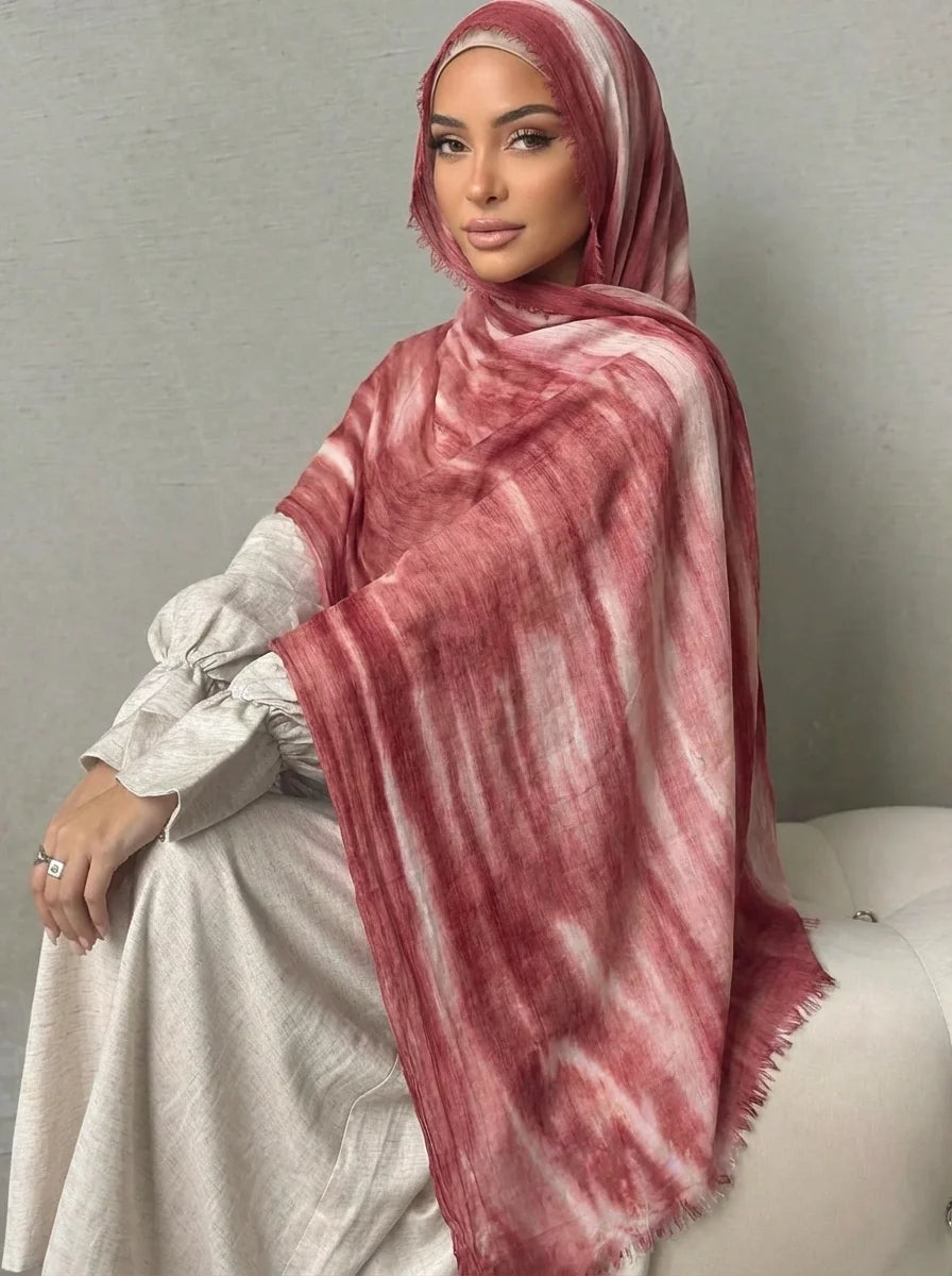 Una mujer vistiendo un pañuelo de hijab a rayas rosadas y rojizas sobre una prenda de color claro.
