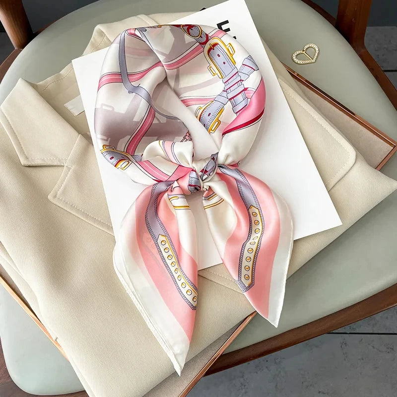 A pink and white silk scarf tied in a bow is displayed on a light beige fabric next to a white card.