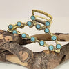 Gold metal hair claw clips decorated with turquoise beads resting on a piece of driftwood.