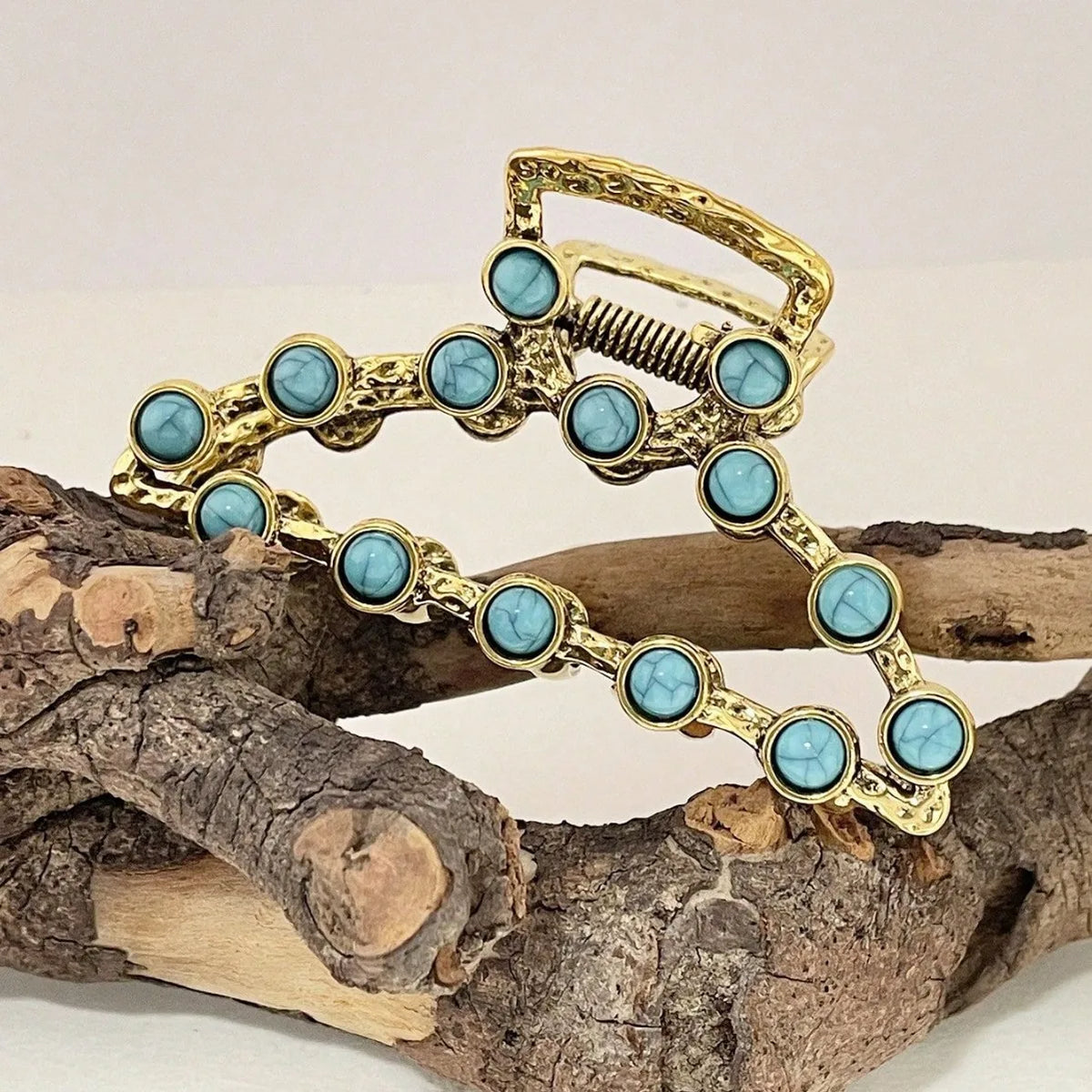 Gold metal hair claw clips decorated with turquoise beads resting on a piece of driftwood.